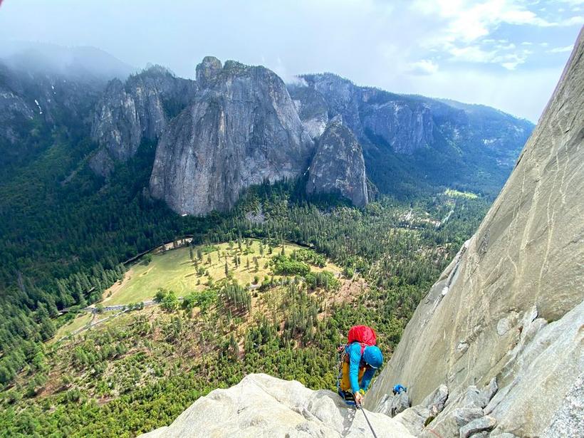 A climber on a granite wall with Yosemite Valley far below